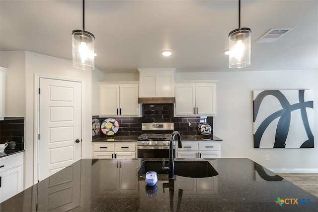 kitchen with hanging light fixtures, dark stone counters, stainless steel gas stove, and white cabinets