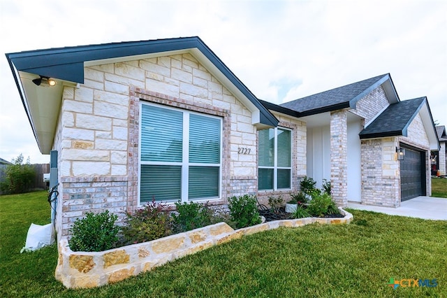 view of front facade with driveway, a shingled roof, stone siding, an attached garage, and a front lawn