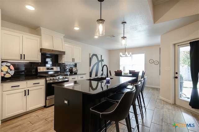 kitchen featuring an island with sink, stainless steel range with gas stovetop, a healthy amount of sunlight, and pendant lighting