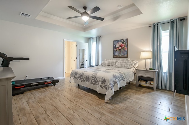 bedroom with light hardwood / wood-style flooring, ceiling fan, crown molding, and a tray ceiling