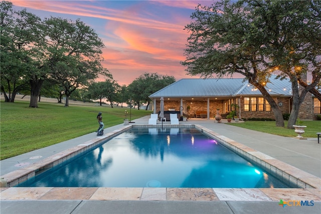 pool at dusk with a lawn and a patio area