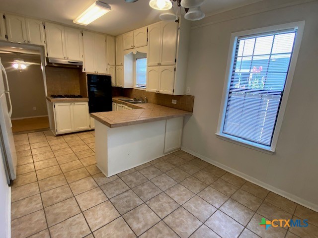 720 S Laurel Ave, Luling, TX 78648 - kitchen with light tile patterned flooring, under cabinet range hood, a peninsula, and white cabinets