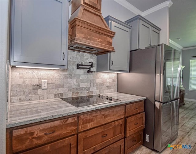 kitchen with light stone countertops, black electric cooktop, custom exhaust hood, backsplash, and ornamental molding