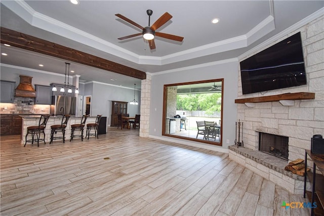 living area with a ceiling fan, a stone fireplace, light wood-style flooring, and a raised ceiling