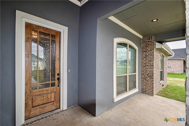 doorway to property featuring brick siding, stucco siding, and a patio area