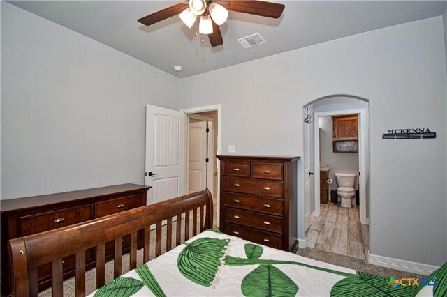 bedroom featuring visible vents, ensuite bathroom, arched walkways, baseboards, and a ceiling fan