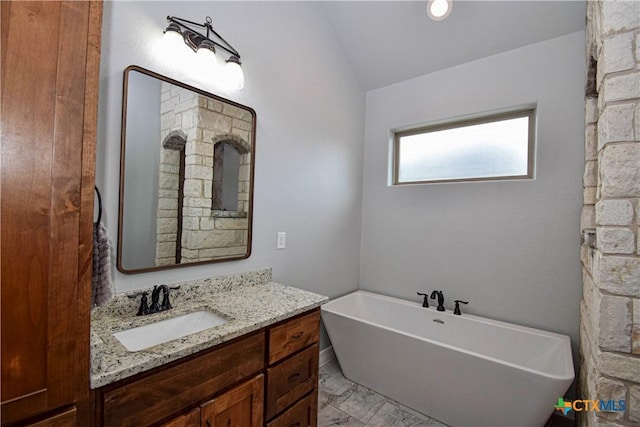 bathroom with marble finish floor, a freestanding tub, vaulted ceiling, and vanity