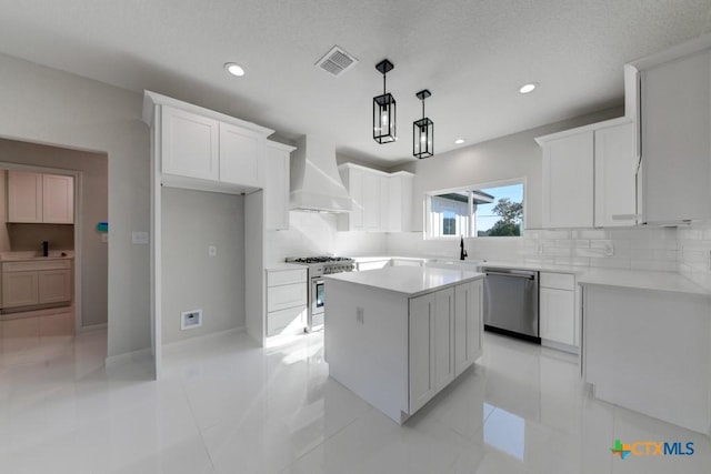 kitchen featuring white cabinetry, hanging light fixtures, stainless steel appliances, a kitchen island, and custom range hood