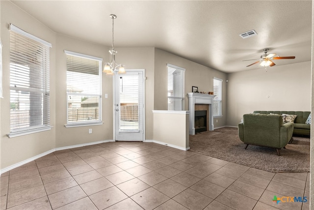 unfurnished living room featuring ceiling fan with notable chandelier, a tiled fireplace, a textured ceiling, and tile patterned floors