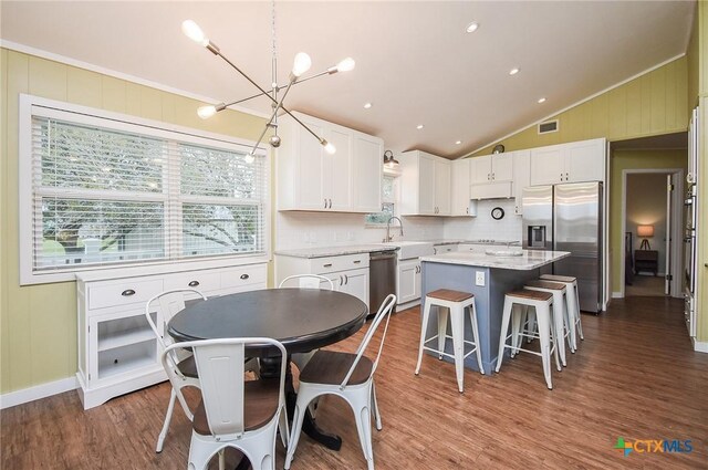 kitchen featuring appliances with stainless steel finishes, decorative light fixtures, white cabinets, a kitchen island, and lofted ceiling