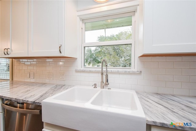 kitchen with dishwasher, light stone counters, white cabinetry, and sink