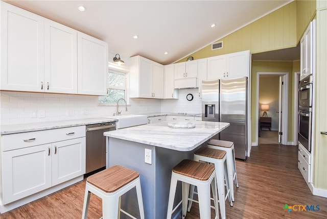 kitchen with stainless steel appliances, sink, white cabinets, a kitchen island, and a breakfast bar area