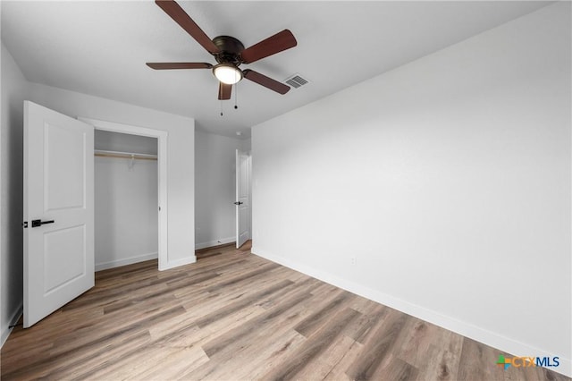 unfurnished bedroom featuring ceiling fan, wood finished floors, visible vents, baseboards, and a closet