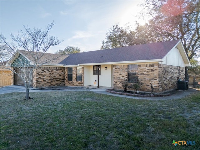 ranch-style house with brick siding, roof with shingles, a garage, cooling unit, and a front lawn