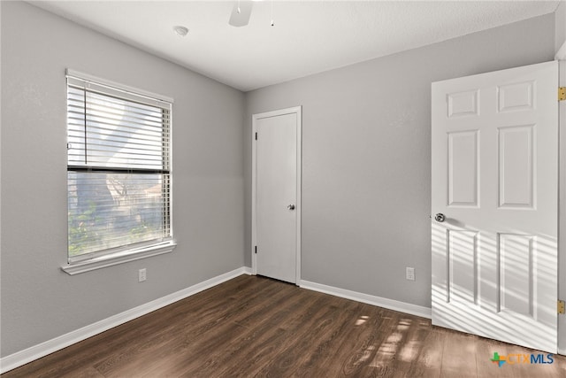 spare room with a ceiling fan, baseboards, and dark wood-type flooring