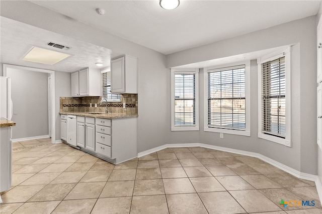 kitchen featuring backsplash, light tile patterned flooring, a sink, and baseboards