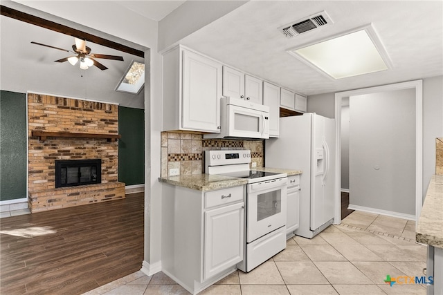 kitchen featuring white appliances, visible vents, white cabinets, decorative backsplash, and a brick fireplace