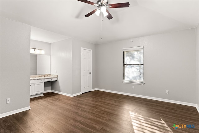 unfurnished bedroom featuring built in desk, dark wood-type flooring, ensuite bath, and baseboards