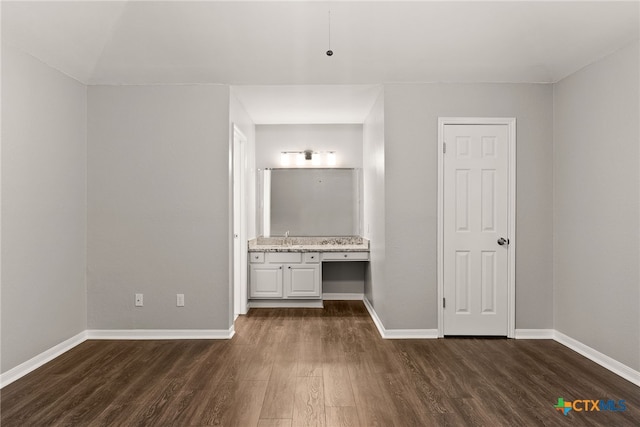 unfurnished bedroom featuring a sink, dark wood finished floors, baseboards, and ensuite bathroom