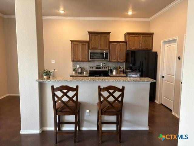 kitchen with light stone counters, appliances with stainless steel finishes, a kitchen breakfast bar, kitchen peninsula, and backsplash