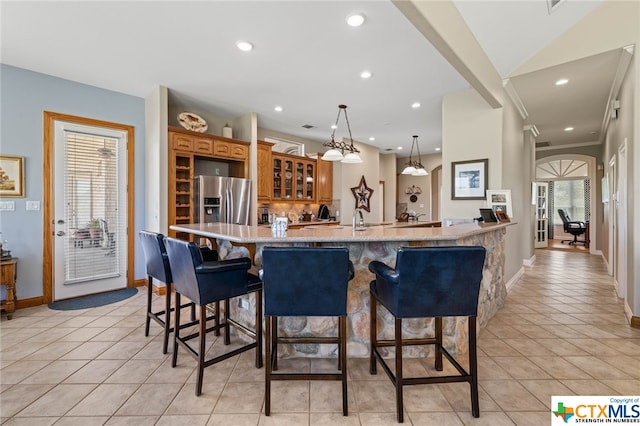 kitchen with decorative light fixtures, light stone countertops, stainless steel fridge with ice dispenser, and a kitchen breakfast bar