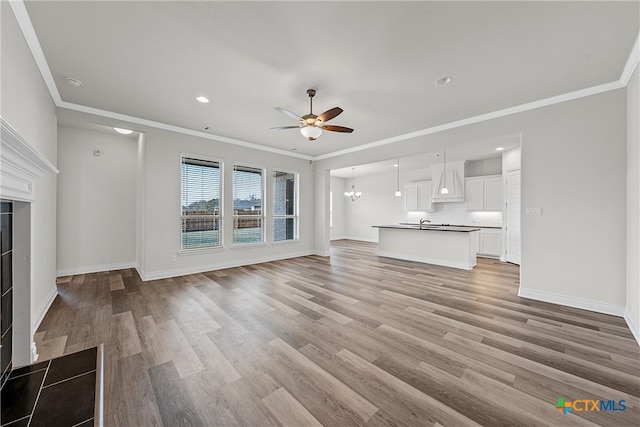 unfurnished living room featuring sink, ceiling fan with notable chandelier, light hardwood / wood-style floors, and crown molding