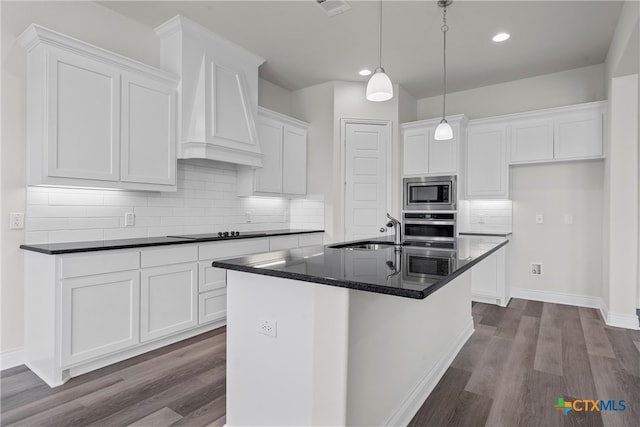 kitchen with a center island with sink, white cabinetry, appliances with stainless steel finishes, decorative backsplash, and hardwood / wood-style flooring