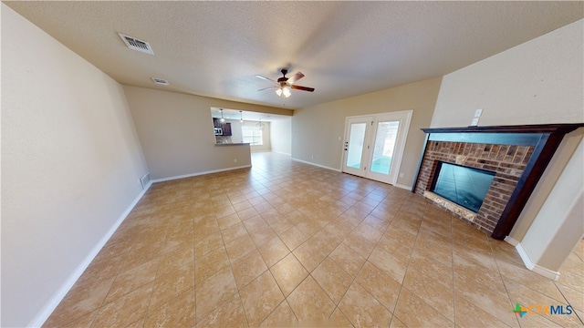 unfurnished living room with a brick fireplace, a textured ceiling, ceiling fan, and light tile patterned floors