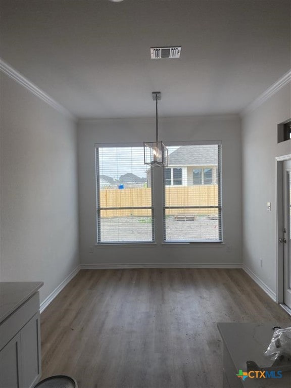 unfurnished dining area with baseboards, visible vents, wood finished floors, and ornamental molding