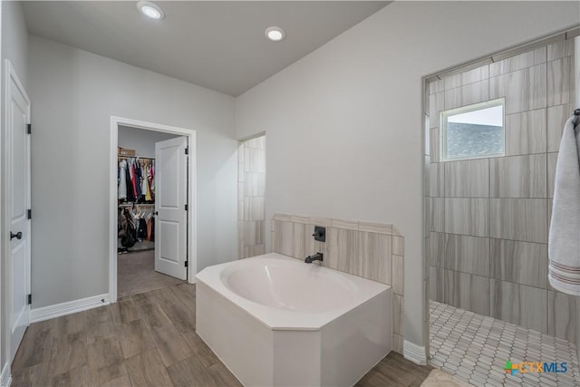 full bath with wood finished floors, a walk in shower, a spacious closet, and a bath