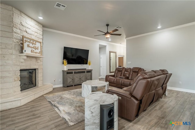 living area with visible vents, a ceiling fan, a stone fireplace, wood finished floors, and baseboards