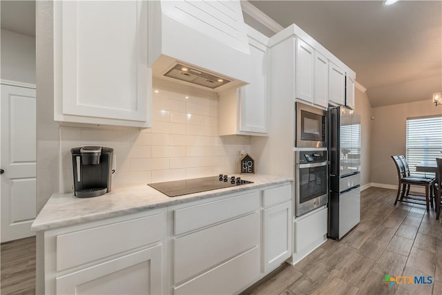 kitchen featuring light wood finished floors, decorative backsplash, appliances with stainless steel finishes, white cabinets, and premium range hood