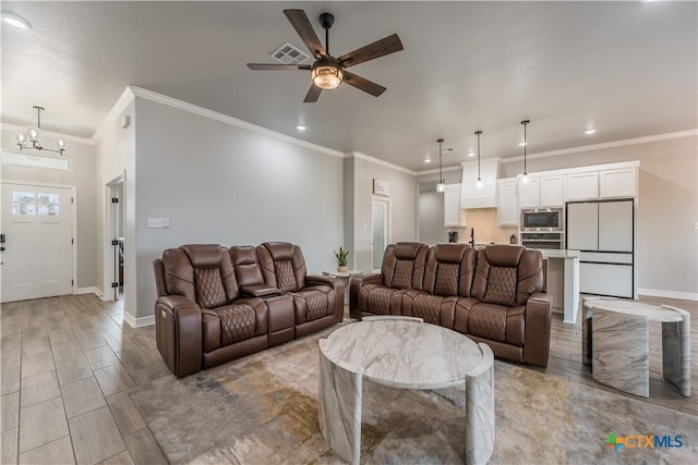 living area featuring baseboards, visible vents, wood finished floors, crown molding, and ceiling fan with notable chandelier