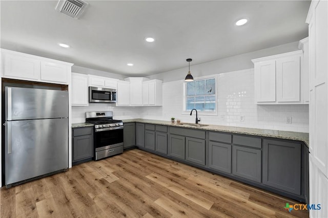 kitchen featuring gray cabinetry, a sink, stainless steel appliances, light wood-style floors, and white cabinets