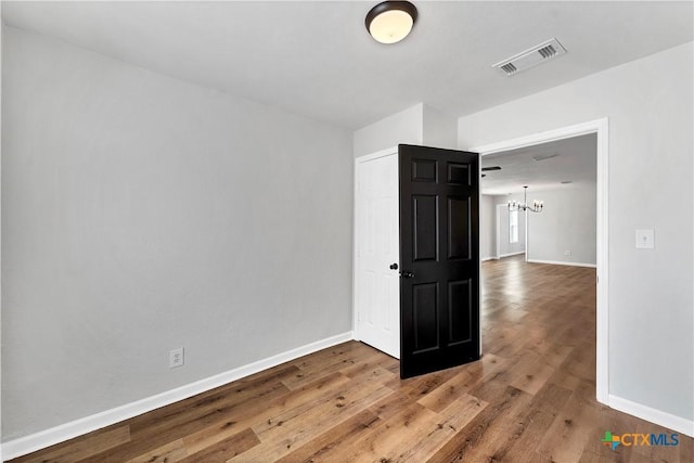 unfurnished room featuring a notable chandelier, visible vents, baseboards, and wood finished floors