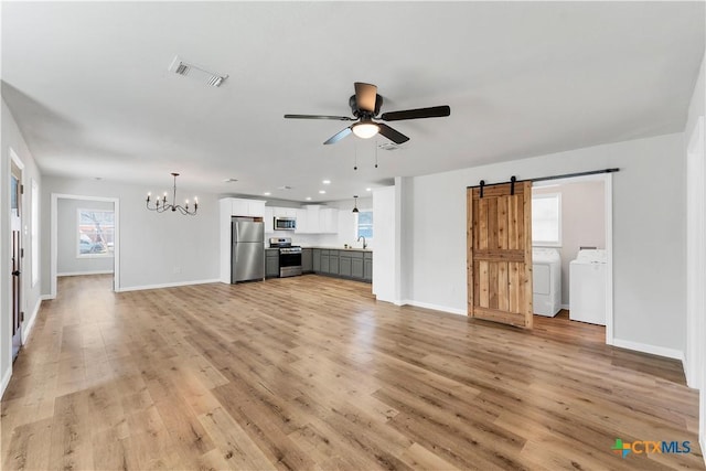 unfurnished living room with visible vents, light wood-style flooring, ceiling fan with notable chandelier, washer and clothes dryer, and a barn door