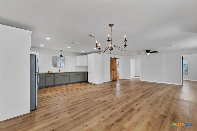 unfurnished dining area with a barn door, ceiling fan with notable chandelier, visible vents, and light wood-type flooring