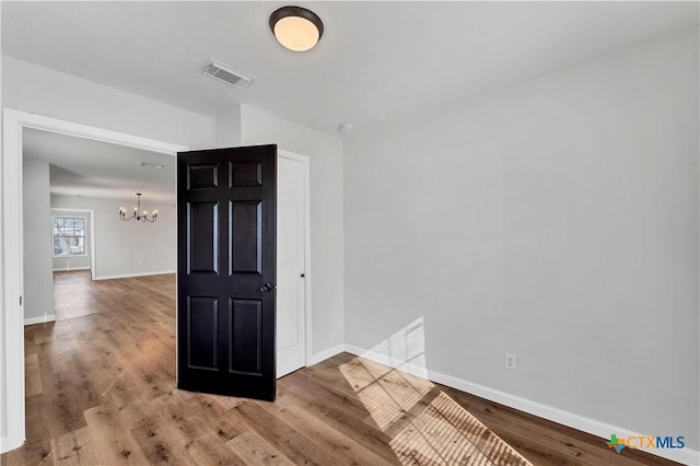 empty room featuring an inviting chandelier, wood finished floors, visible vents, and baseboards