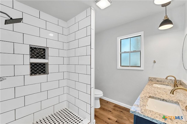 full bathroom featuring a sink, toilet, wood finished floors, and a tile shower