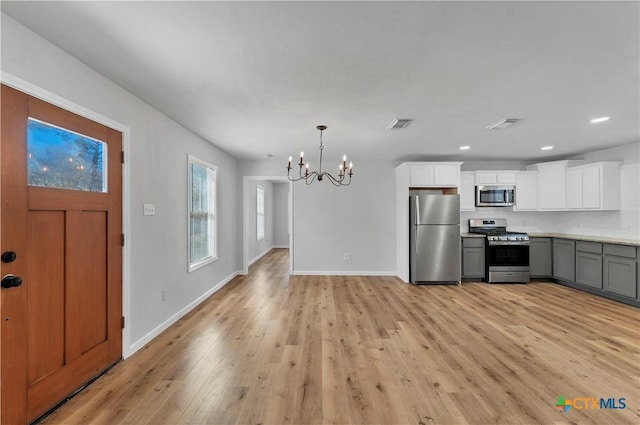 kitchen featuring visible vents, light wood-type flooring, stainless steel appliances, an inviting chandelier, and white cabinetry