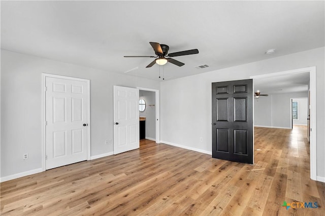 unfurnished bedroom featuring light wood finished floors, visible vents, baseboards, attic access, and a ceiling fan