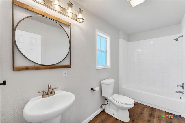 bathroom with baseboards, toilet, bathtub / shower combination, wood finished floors, and a sink