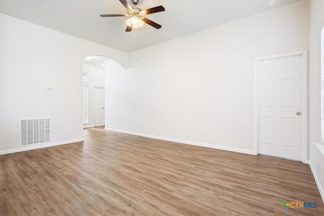 spare room with baseboards, arched walkways, light wood finished floors, ceiling fan, and visible vents