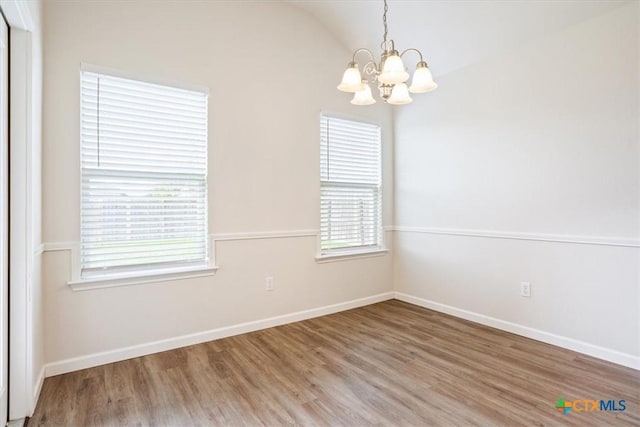 spare room with lofted ceiling, baseboards, a chandelier, and wood finished floors