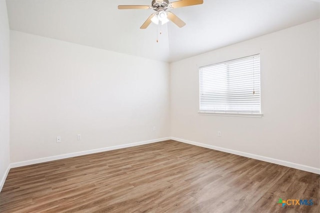 unfurnished room featuring baseboards, ceiling fan, wood finished floors, and vaulted ceiling