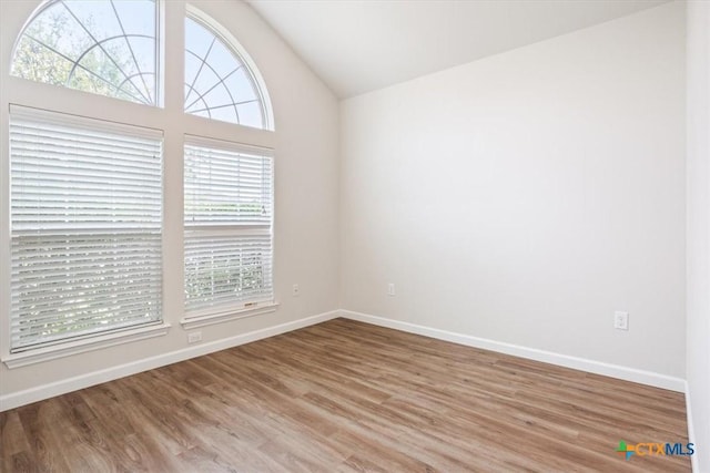 empty room with baseboards, wood finished floors, and vaulted ceiling
