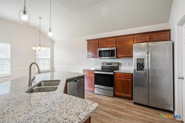 kitchen with lofted ceiling, stainless steel appliances, a sink, light wood-style flooring, and a notable chandelier