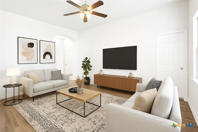 living area featuring a ceiling fan, arched walkways, baseboards, and wood finished floors