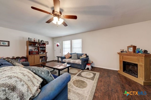 living area featuring a ceiling fan, a glass covered fireplace, baseboards, and wood finished floors