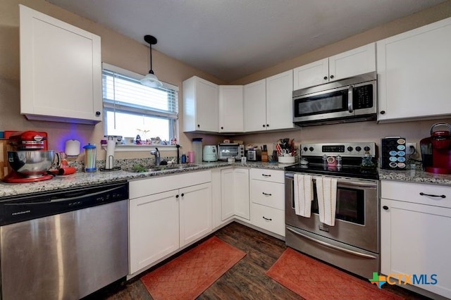 kitchen with appliances with stainless steel finishes, dark wood-type flooring, white cabinets, a sink, and light stone countertops